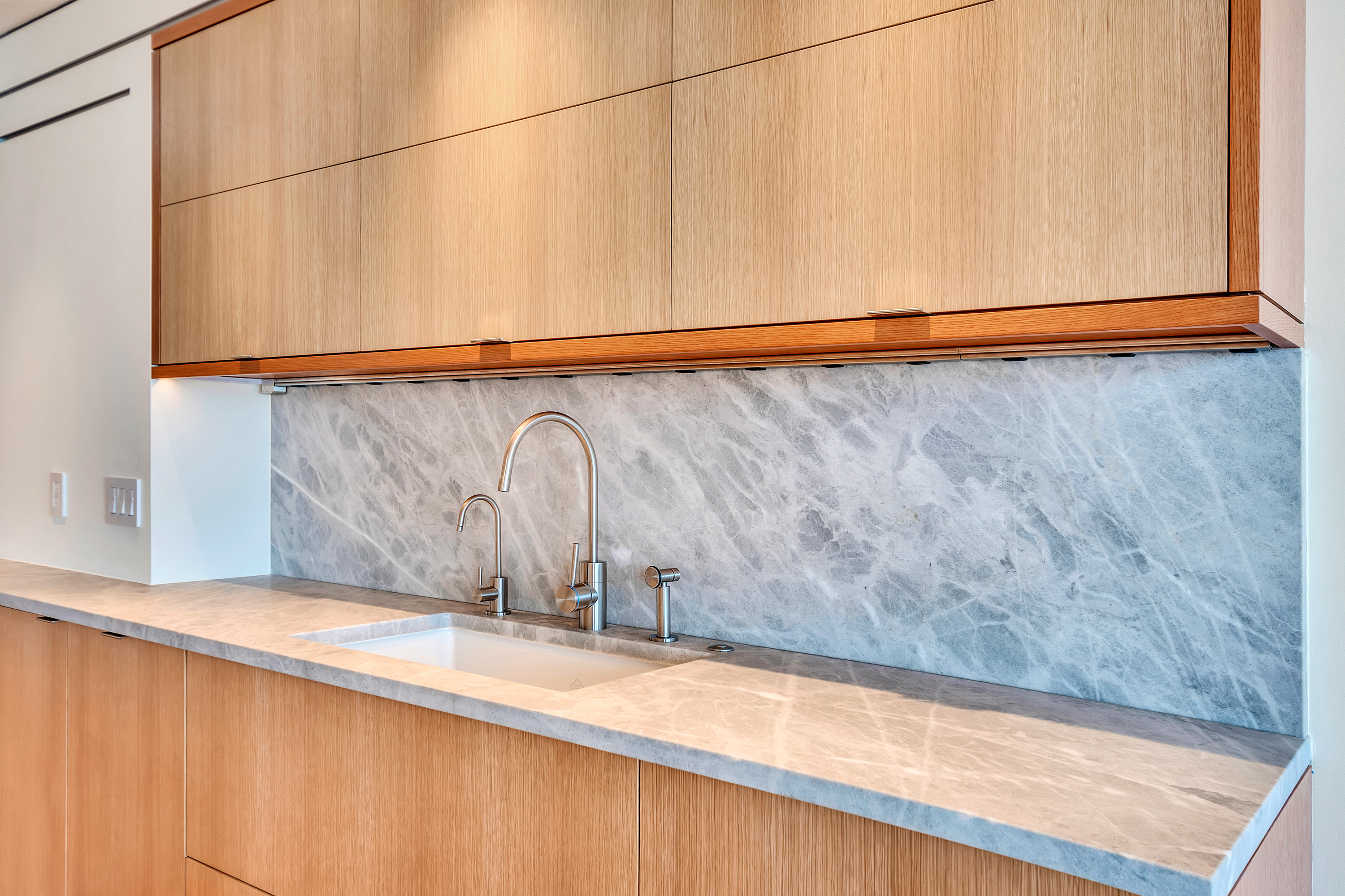 Kitchen cabinetry, stone backsplash, and integrated lighting detail