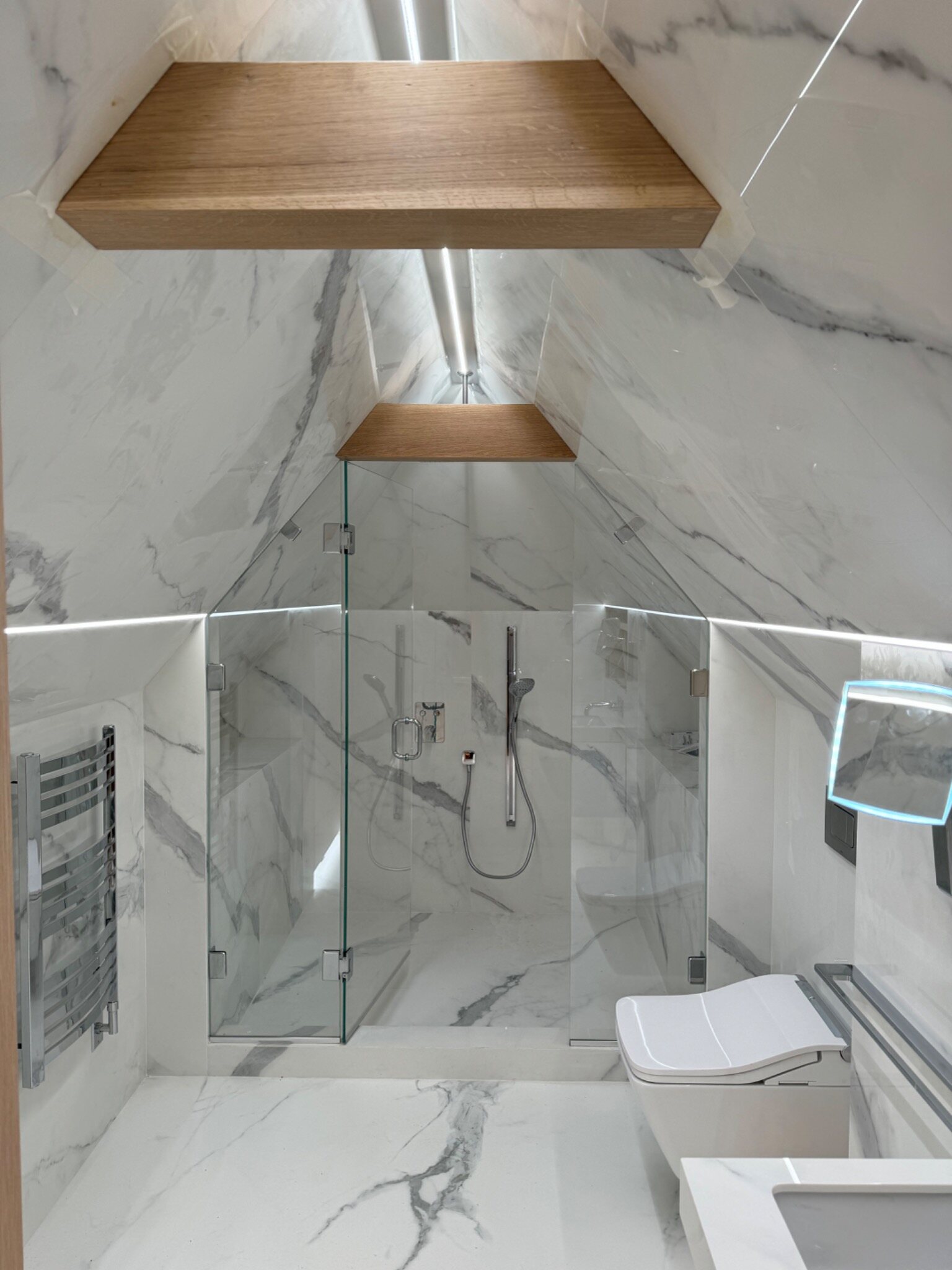 Completed marble bathroom with glass shower and integrated lighting
